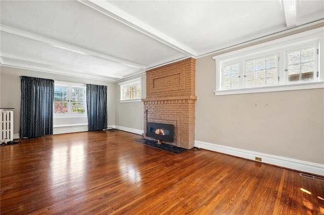 unfurnished living room with radiator heating unit, wood finished floors, visible vents, beam ceiling, and a brick fireplace