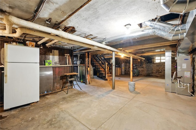 below grade area featuring freestanding refrigerator, stairway, and heating unit