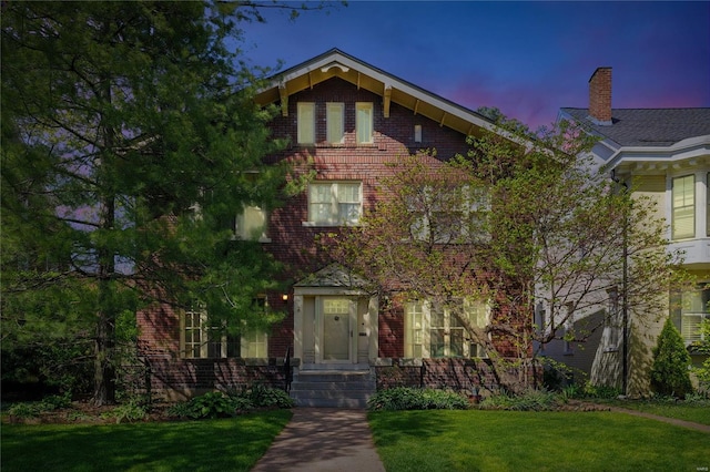 view of front of home featuring a lawn, brick siding, and a chimney