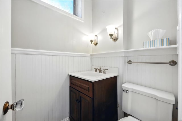 half bathroom with wainscoting, toilet, and vanity