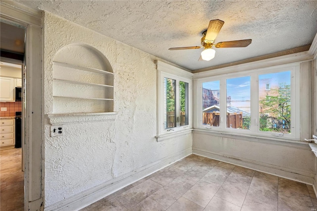 spare room with a textured wall, a textured ceiling, a ceiling fan, and baseboards