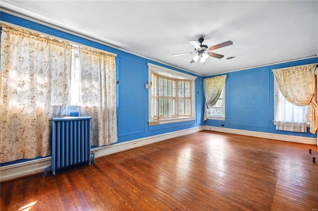 empty room featuring radiator, plenty of natural light, baseboards, ceiling fan, and hardwood / wood-style flooring