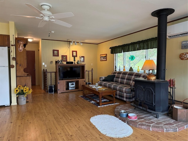 living room with ceiling fan, light wood finished floors, a wood stove, an AC wall unit, and rail lighting