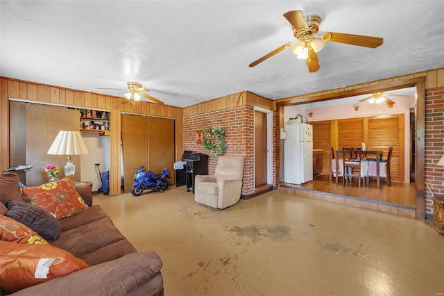 living area featuring concrete flooring, wooden walls, brick wall, and ceiling fan
