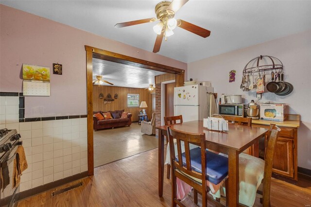 dining room featuring wood finished floors, visible vents, wooden walls, and ceiling fan