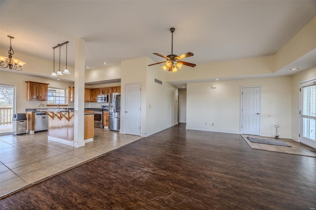 unfurnished living room with baseboards, wood finished floors, visible vents, and ceiling fan with notable chandelier