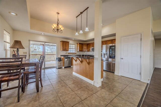 kitchen with a kitchen breakfast bar, brown cabinetry, a chandelier, a wealth of natural light, and appliances with stainless steel finishes