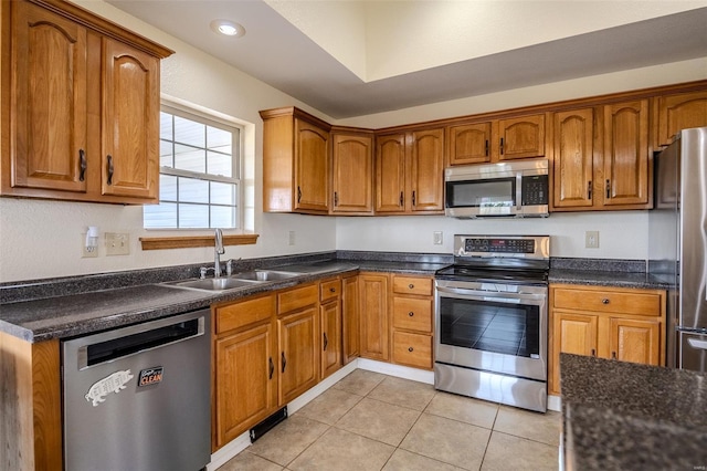 kitchen with brown cabinetry, appliances with stainless steel finishes, a sink, and light tile patterned flooring