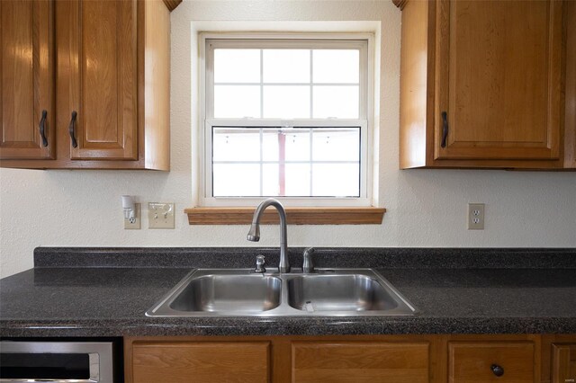 kitchen featuring brown cabinetry, a sink, and dark countertops