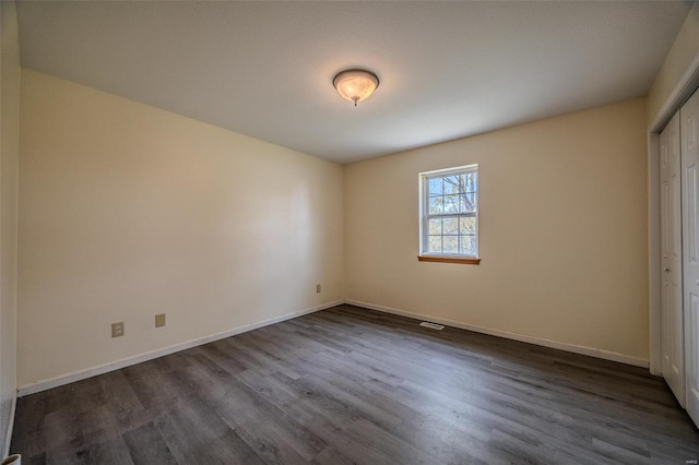 unfurnished bedroom featuring visible vents, baseboards, dark wood-style floors, and a closet