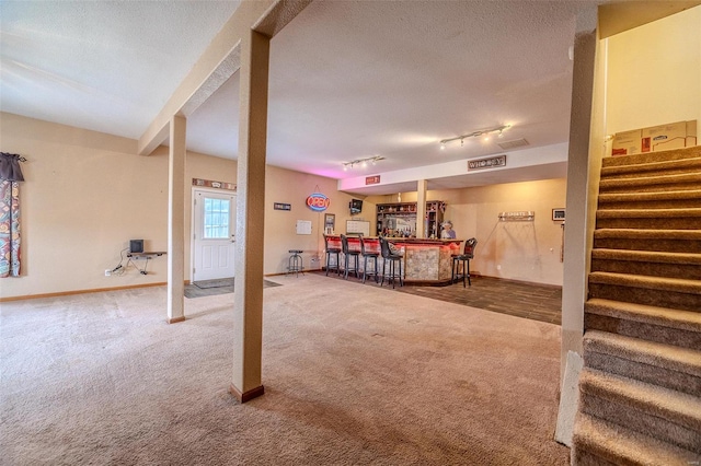 carpeted living area featuring stairway, baseboards, a dry bar, and a textured ceiling