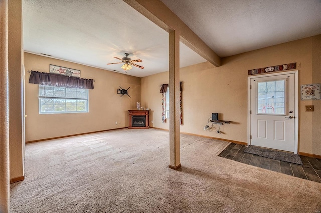 carpeted foyer entrance with a textured ceiling, baseboards, beamed ceiling, ceiling fan, and a fireplace