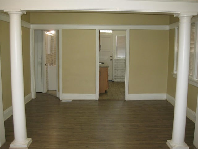 unfurnished bedroom with baseboards, decorative columns, connected bathroom, and dark wood-style floors