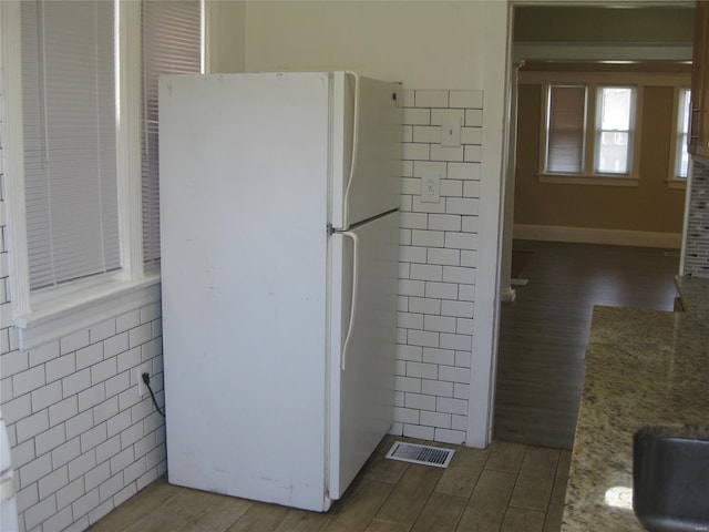 kitchen with wood finished floors, freestanding refrigerator, visible vents, and tile walls