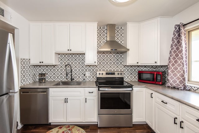 kitchen with wall chimney range hood, decorative backsplash, appliances with stainless steel finishes, a sink, and white cabinets