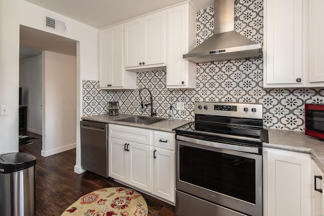 kitchen with wall chimney range hood, appliances with stainless steel finishes, a sink, visible vents, and dark wood-style floors