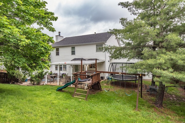 rear view of property with a chimney, a trampoline, a playground, a yard, and a patio