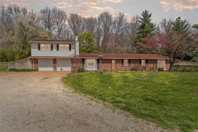 traditional home featuring a chimney, driveway, brick siding, a garage, and a yard