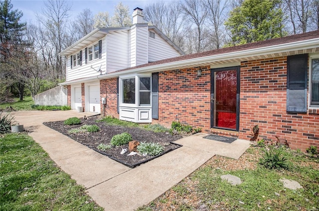 view of front of house featuring a chimney, a garage, driveway, and brick siding
