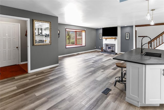 living room with a large fireplace, visible vents, wood finished floors, stairs, and baseboards
