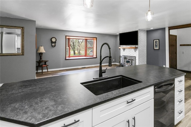 kitchen featuring black dishwasher, a brick fireplace, a sink, dark countertops, and light wood-style flooring