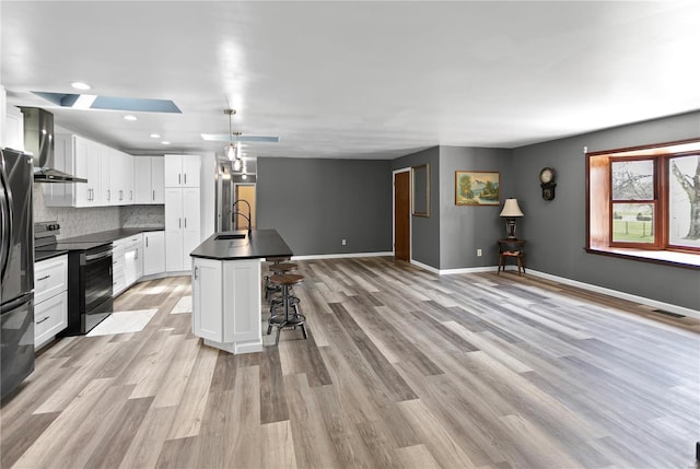 kitchen with baseboards, dark countertops, wall chimney exhaust hood, range with electric cooktop, and a sink