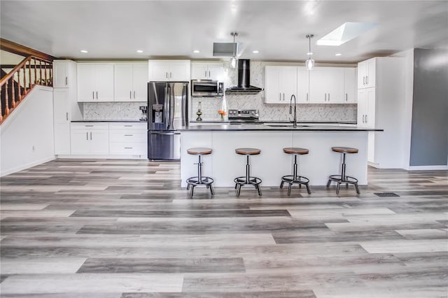 kitchen featuring appliances with stainless steel finishes, wall chimney range hood, dark countertops, a skylight, and a sink