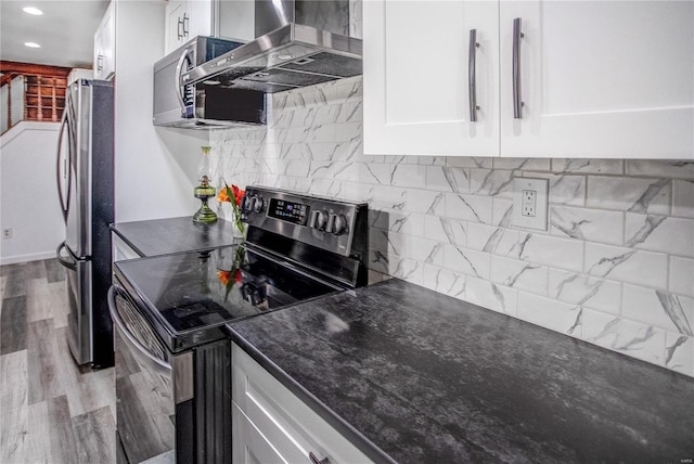 kitchen featuring tasteful backsplash, wall chimney exhaust hood, dark countertops, white cabinetry, and stainless steel appliances
