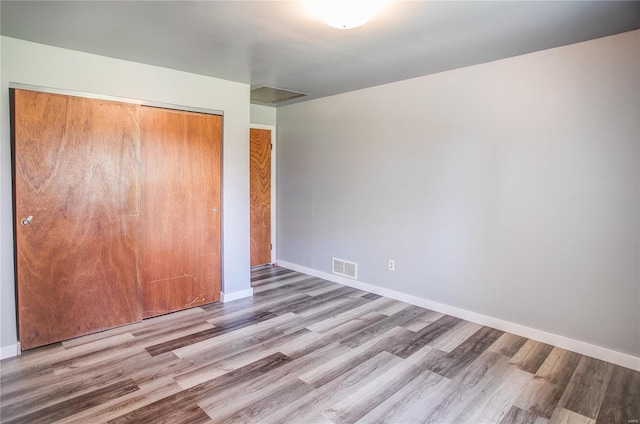 unfurnished bedroom with a closet, wood finished floors, baseboards, and visible vents