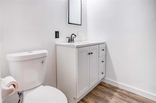 half bath featuring toilet, vanity, wood finished floors, and baseboards