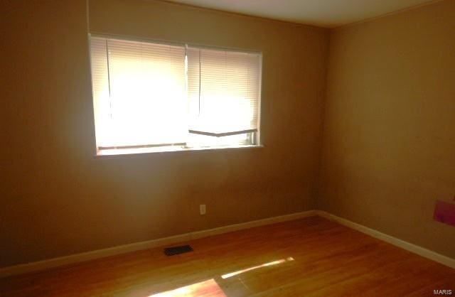 empty room featuring baseboards, wood finished floors, and visible vents