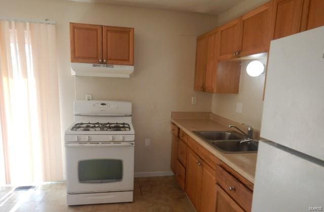 kitchen with white appliances, range hood, light countertops, brown cabinets, and a sink