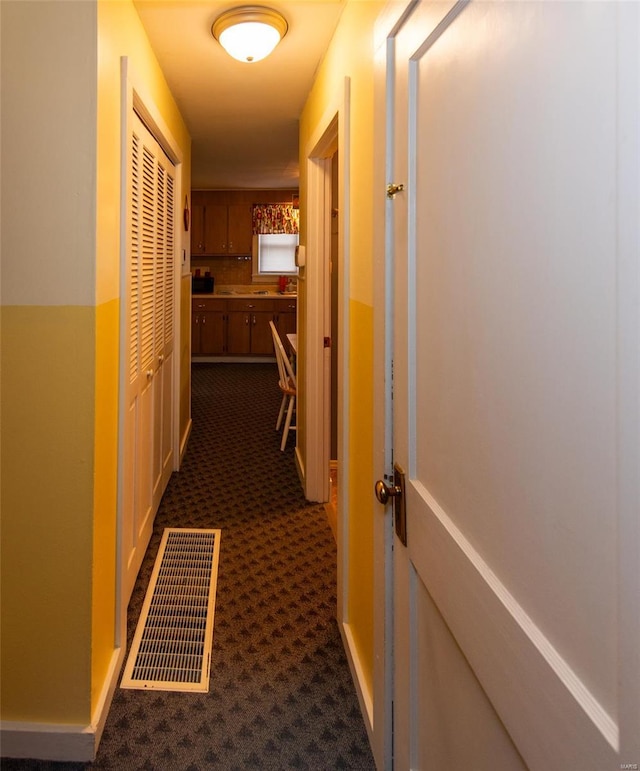 hallway with baseboards, dark colored carpet, and visible vents