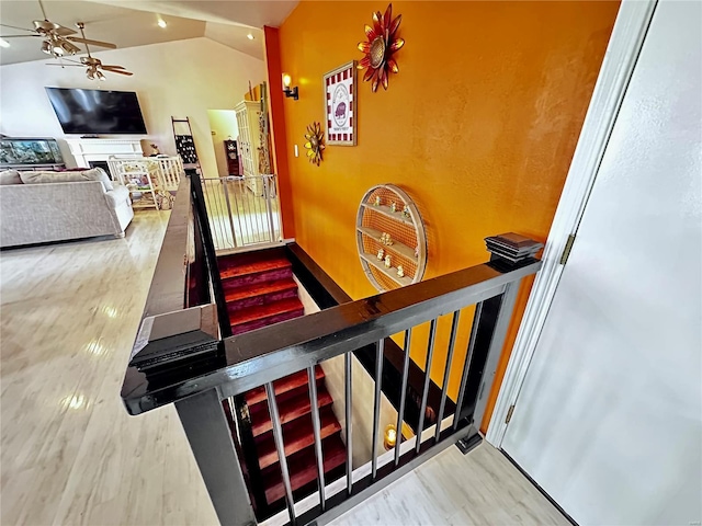 staircase with ceiling fan, vaulted ceiling, wood finished floors, and a fireplace