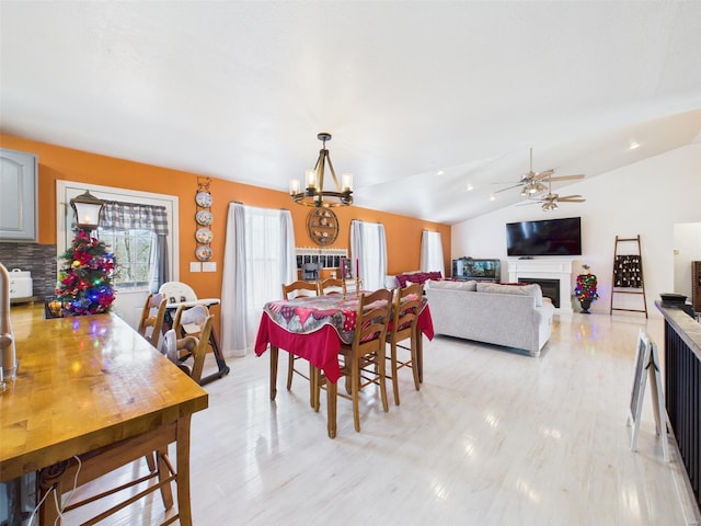 dining room with light wood-style floors, ceiling fan with notable chandelier, a fireplace, and vaulted ceiling