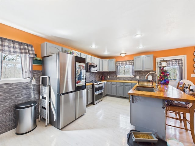 kitchen with a sink, a peninsula, stainless steel appliances, gray cabinets, and a breakfast bar area