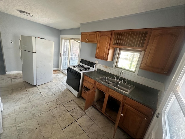 kitchen featuring brown cabinets, dark countertops, a sink, white appliances, and decorative backsplash