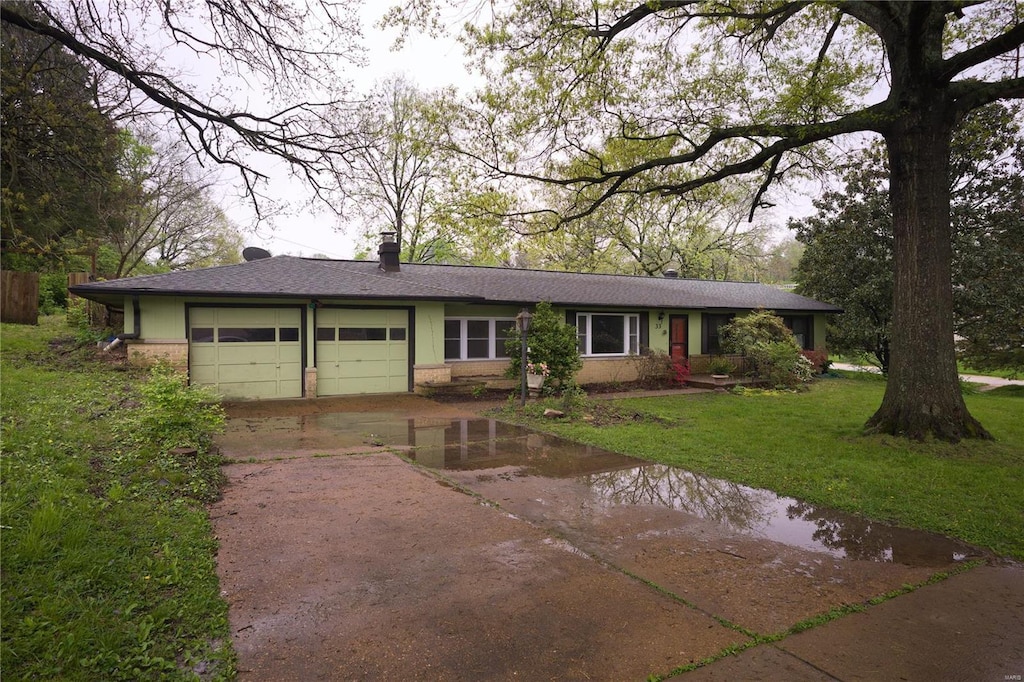 ranch-style house featuring roof with shingles, concrete driveway, a garage, brick siding, and a front yard