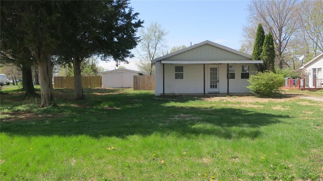 rear view of property with a shed, a yard, fence, and an outbuilding