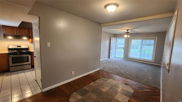 interior space with brown cabinetry, a ceiling fan, under cabinet range hood, stainless steel gas range, and baseboards