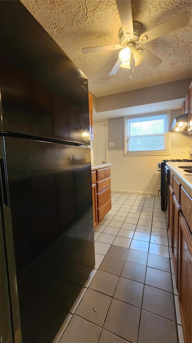 kitchen featuring light tile patterned floors, ventilation hood, freestanding refrigerator, a textured ceiling, and brown cabinetry