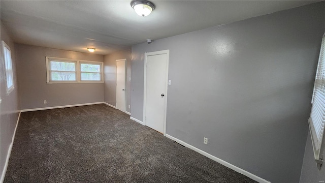 unfurnished room featuring dark colored carpet and baseboards