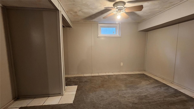 below grade area with light carpet, light tile patterned floors, and ceiling fan