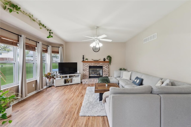 living area featuring visible vents, ceiling fan, a brick fireplace, and light wood-style floors