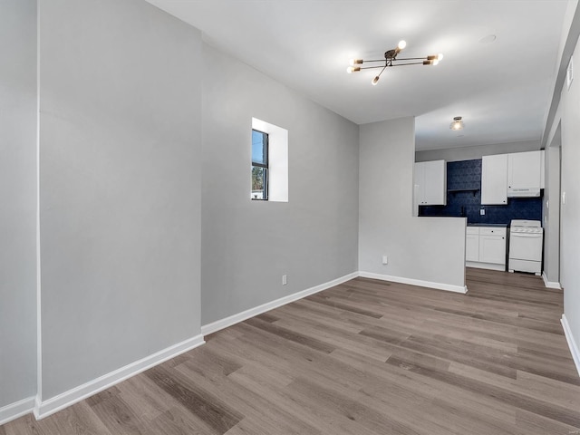 unfurnished living room with a notable chandelier, baseboards, and light wood-type flooring