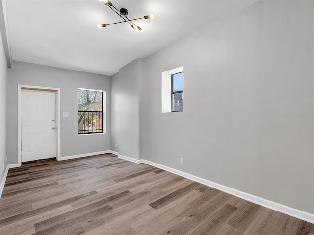 empty room with wood finished floors, a chandelier, and baseboards