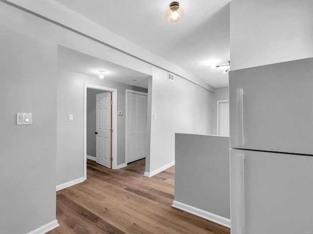 hallway featuring visible vents, wood finished floors, and baseboards
