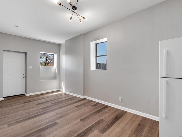 empty room with baseboards, wood finished floors, and a notable chandelier