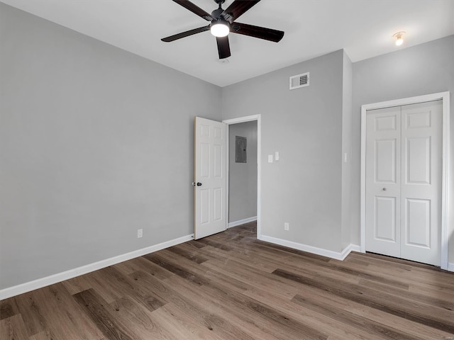 unfurnished bedroom with wood finished floors, a closet, electric panel, baseboards, and visible vents