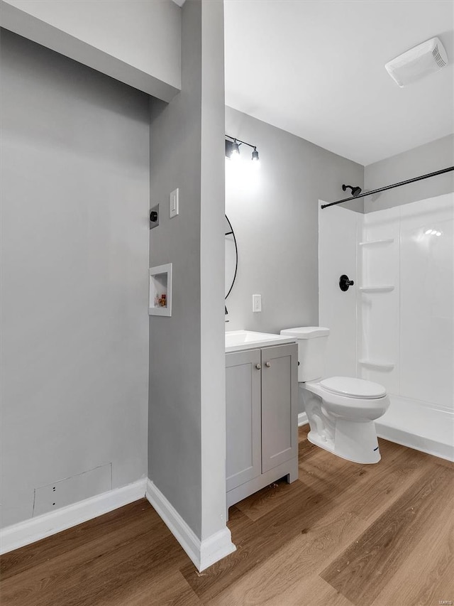 bathroom featuring wood finished floors, walk in shower, toilet, and vanity